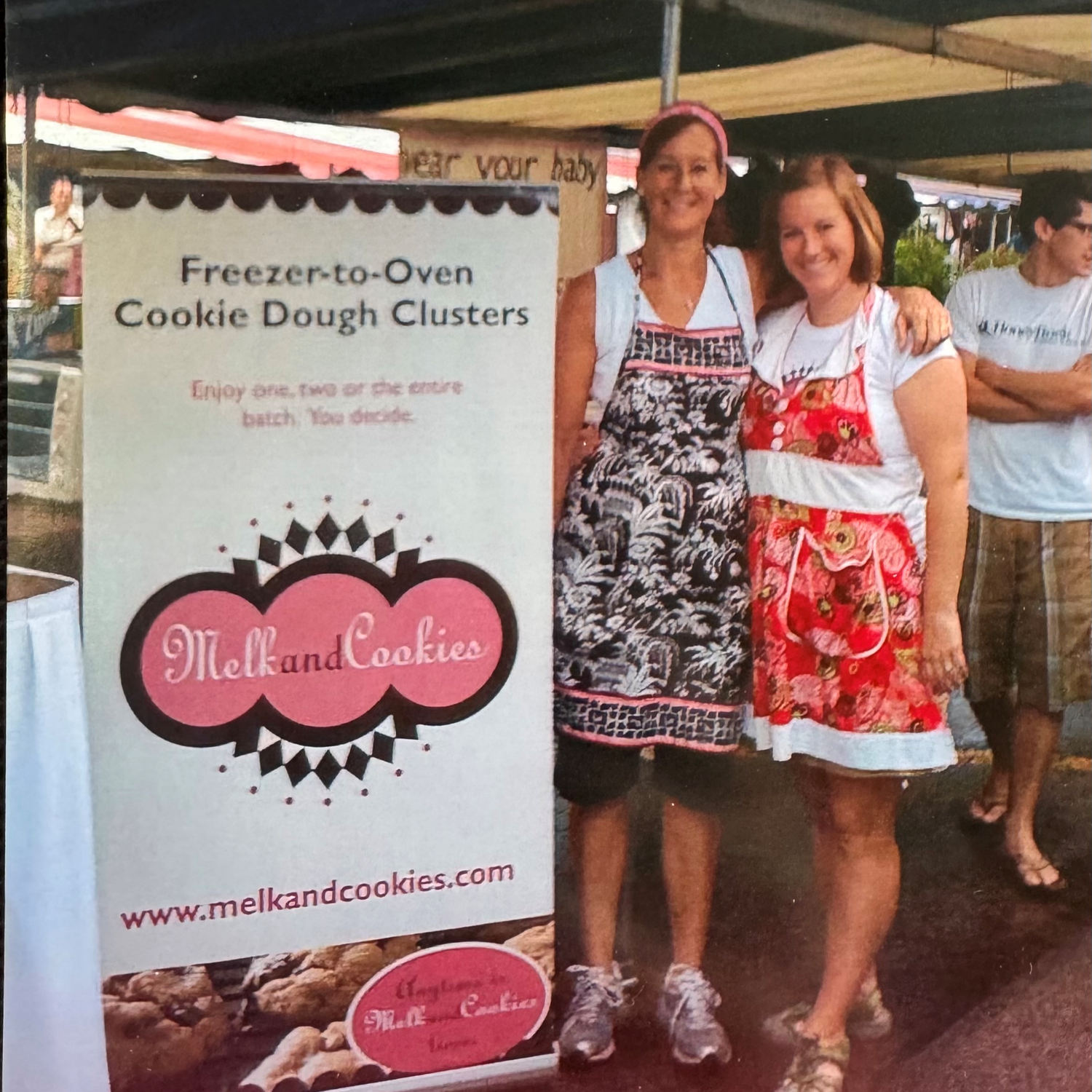 Two women standing next to a Melkand Cookies booth at an outdoor event.